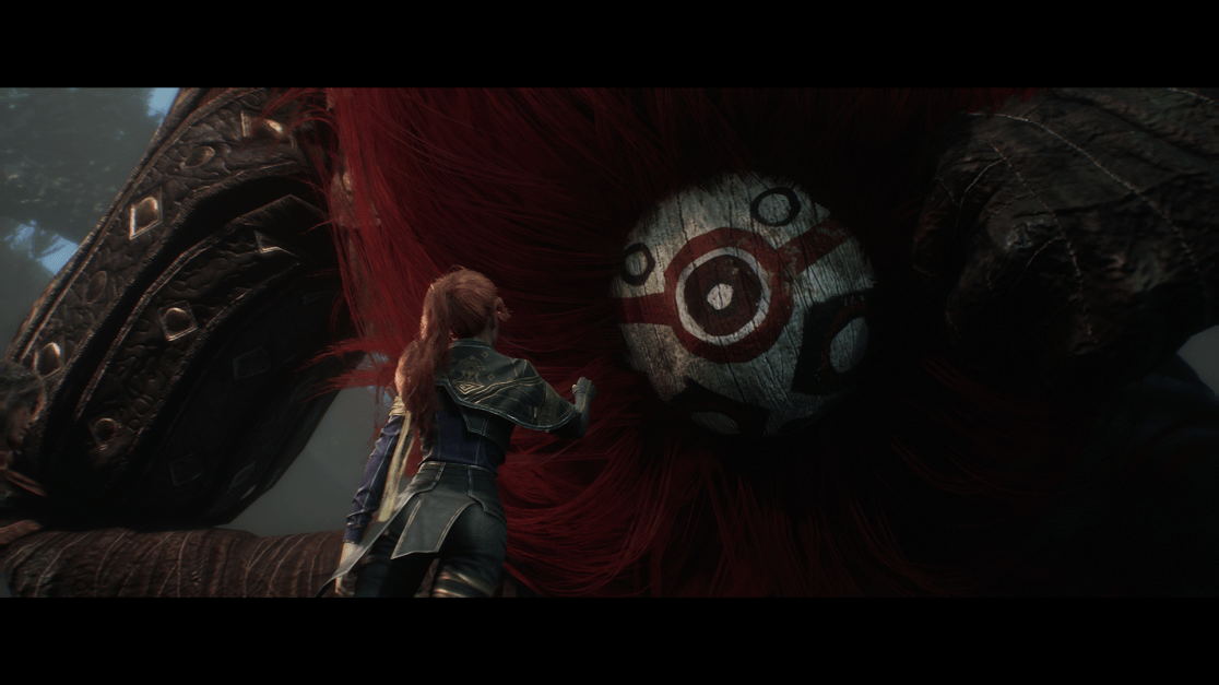 A woman stands looking up at a colossal creature with long, red fur. The creature has a round, painted wooden mask with concentric red and white circles around the eye. The woman wears a dark blue and gold outfit. The creature's large, leather-covered hand and arm are partially visible with detailed quilting. The scene is shadowy, giving a sense of danger and mystery.