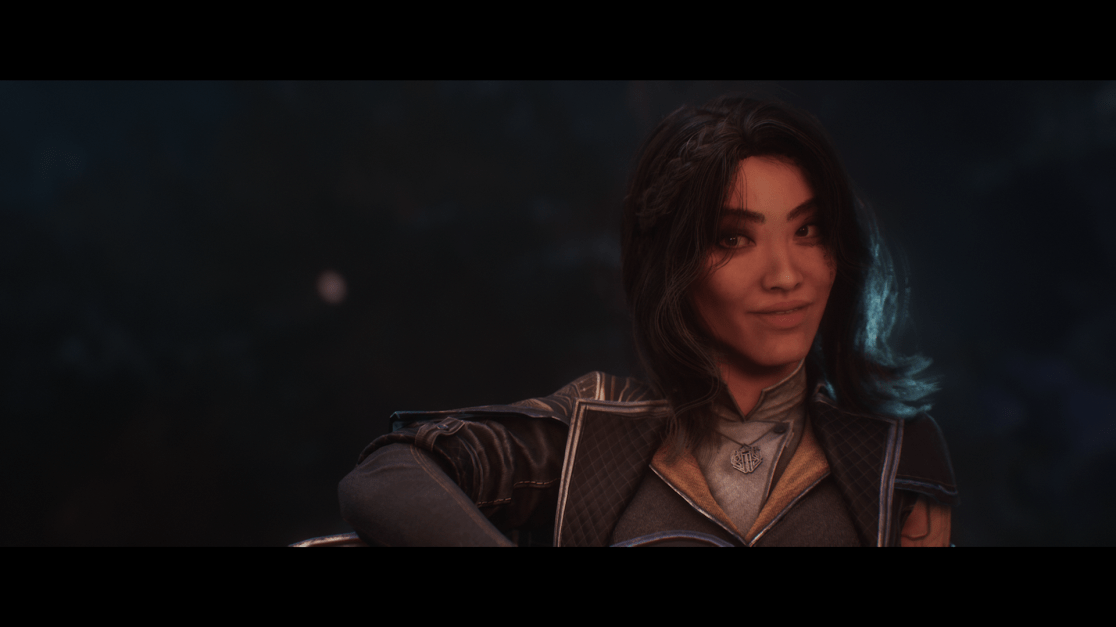 A close-up portrait of a woman with dark, shoulder-length hair styled with loose waves, captured in a dimly lit, atmospheric setting. She has fair skin, is looking directly at the viewer with a slight smile. The woman wears a dark blue, quilted, outer collored piece over a tan shirt. A silver pendant with intricate design hangs around her neck. The backdrop is dark and blurry, indicating a background of night or shadow