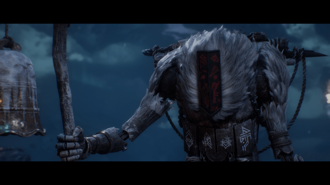 A large, imposing creature stands partially obscured in a low-lit, nighttime setting. The creature has grey fur, a dark banner attached to its back with red symbols, and stylized armor plates with carved symbols around its midsection. It holds a thick wooden staff with a bell hanging from it.