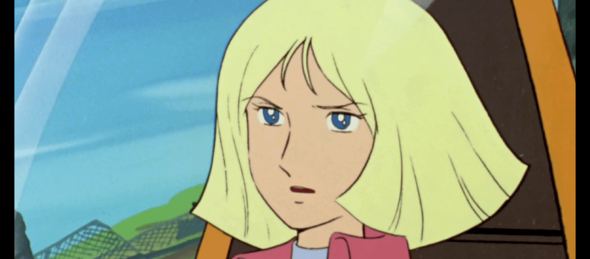 An animated female character with blonde, shoulder-length hair and piercing blue eyes exhibits a worried or apprehensive expression. She has fair skin and is wearing a pink jacket over a light blue top. The scene is set inside a vehicle, possibly a car or aircraft, as suggested by the windshield view outside the window, revealing a bright blue sky and a glimpse of a green, mesh-like structure. The framing is a close-up, focusing on the woman's facial expression and immediate surroundings.