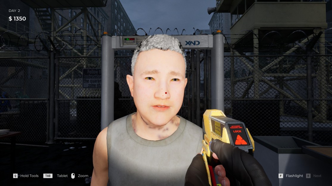 A first-person perspective from a video game shows a gloved hand wielding a yellow scanner, pointed at a pale man with grey hair and yellow eyes. The man stands in front of a security scanner, and a barbed wire fence is visible in the background. Game interface elements show "Day 2" and "$1350" at the top left. Interface options for tools, tablet, zoom,flashlight, and 'next' are displayed along the bottom.