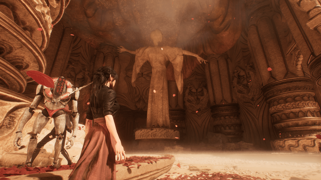 In a temple-like setting, a woman with dark hair stands near the edge of a stone platform covered in red petals, observed by a robot. The woman gazes towards a large statue with outstretched arms standing in the center of an ornately decorated, cave-like structure.