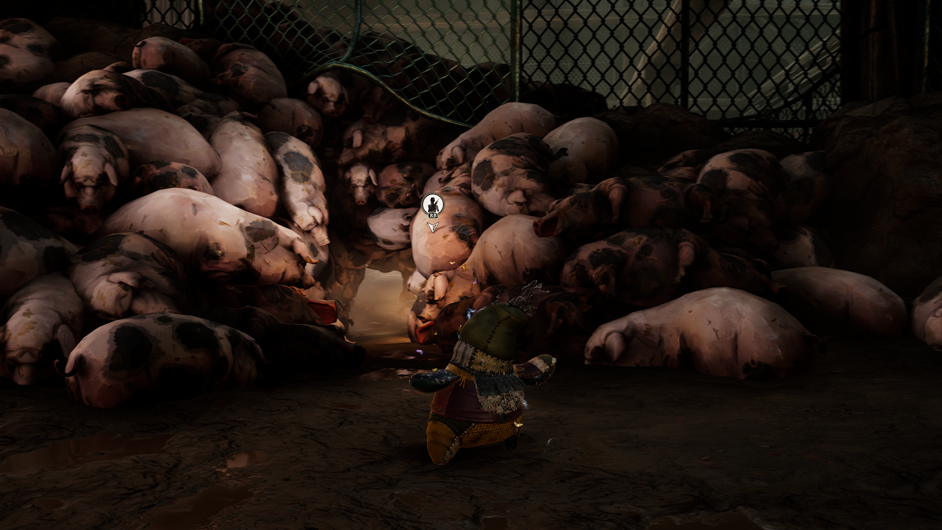 Gameplay screenshot from South of Midnight showing a player character in a patchwork outfit standing before a grotesque tunnel made of pig carcasses. The scene is set in a dark, enclosed area with a chain-link fence in the background, evoking a grim and surreal Southern Gothic atmosphere. The image highlights the game’s narrative-driven horror elements and unique visual storytelling.
