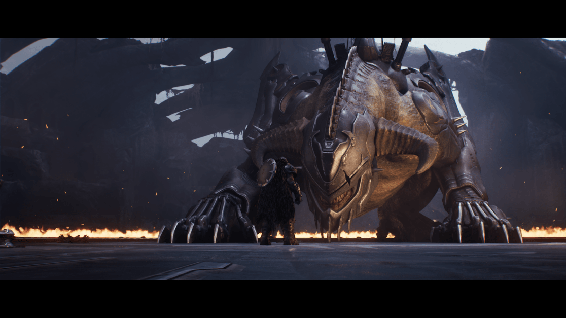 A wide shot features a heavily armored warrior standing before a colossal, dragon-like creature in a dimly lit, cavernous arena. The warrior, seen from the back, is clad in ornate armor with a shield and fur cloak. The massive beast, facing the warrior, is armored with metallic plates and spikes. Its head is menacing with sharp teeth and horns. A line of flames separates the two figures, and the background shows a dark, fortress-like structure with visible damage and crumbling architecture. Sparks float in the air, adding to the dramatic and intense atmosphere of the scene.